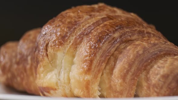 Croissant on white plate rotating in front of camera on black background