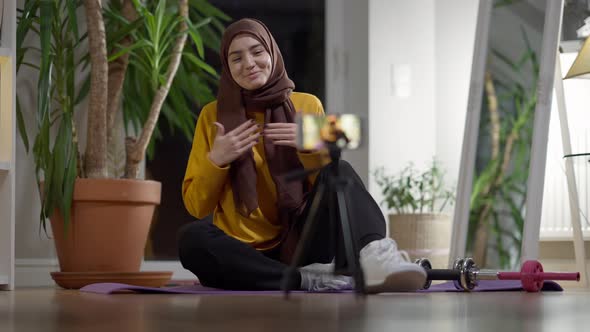 Cheerful Sport Blogger in Hijab Waving and Talking at Smartphone Streaming Online