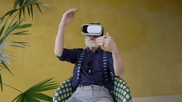 Bearded 70-aged Man which Sitting in the Chair and Using Virtual Reality Headset