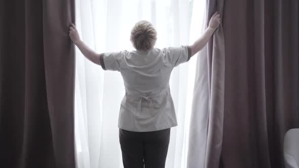 Back View of Professional Hotel Maid Opening Curtains in Hotel Room