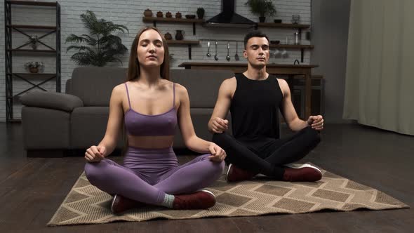 Young Fitness Man and Woman in Sportswear Meditating Doing Yoga on the Floor with Closed Eyes
