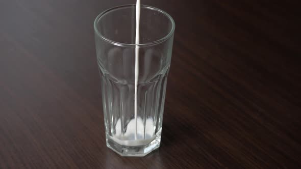 Pouring cow milk into a tall glass on a wooden table