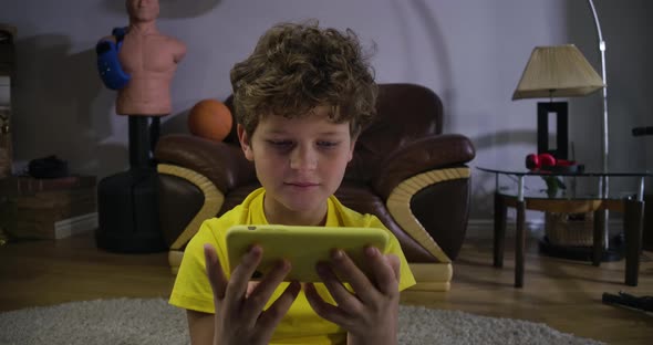 Face of Focused Caucasian Boy Watching Cartoons or Movie on Smartphone Screen. Child with Curly Hair