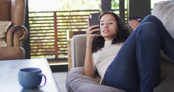 Relaxed biracial woman lying on sofa and using smartphone