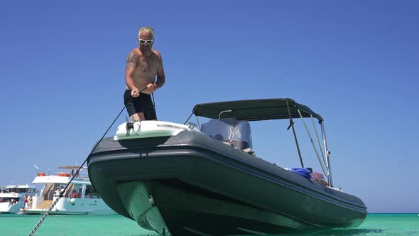 Wide Shot Portrait of Tanned Tattooed Man Pulling Anchor Chain in Slow Motion Standing on Yacht in