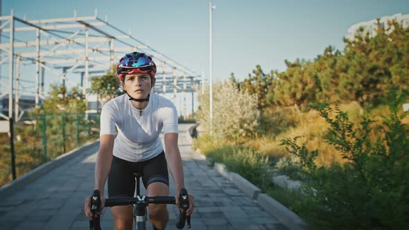 Sportswoman in Protective Helmet is Riding Bicycle Along Tiled Bike Path in a City Park Planted with