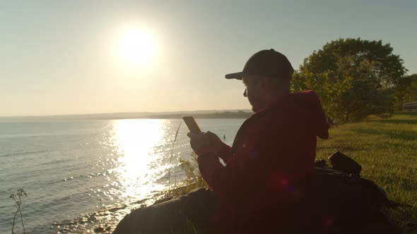 Young Traveler is Browsing His Smartphone While Sitting Beach Ocean