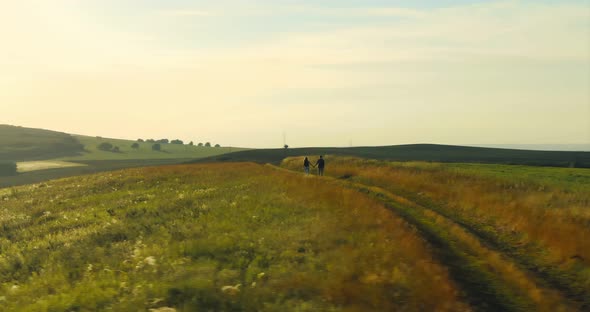 Two Tourists Walk on Hilly Terrain a Panoramic Shot From the Copter