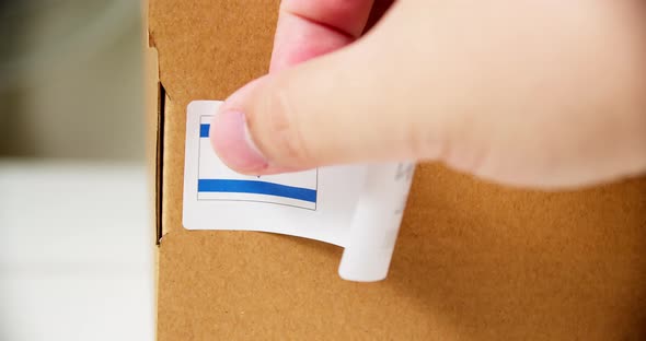 Hands applying MADE IN ISRAEL flag label on a shipping cardboard box with products. Close up shot wi