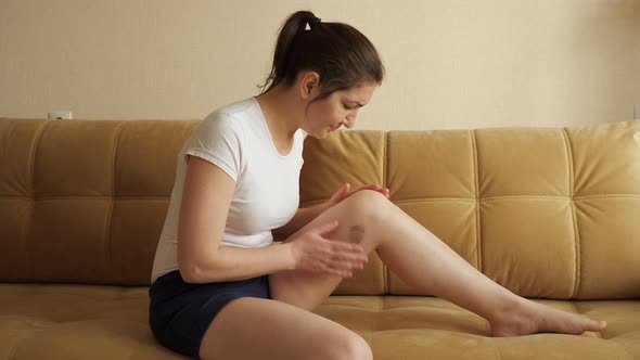 Woman Sitting on the Couch Examines the Injury on Her Leg. Pain