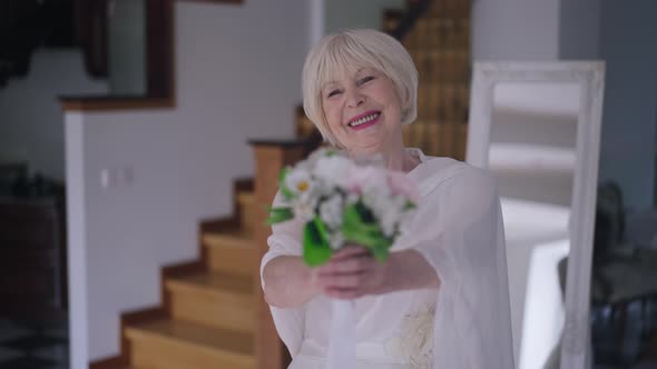 Charming Satisfied Senior Bride in Wedding Dress Stretching Bridal Bouquet Looking at Camera Smiling