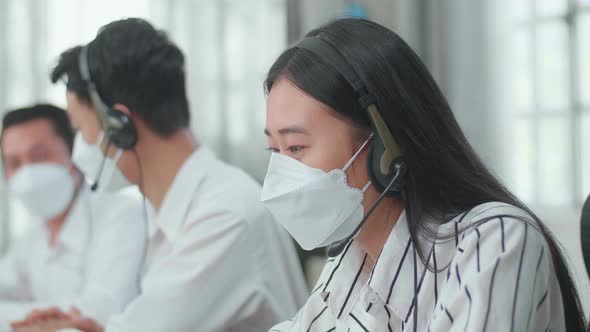 A Woman Of Three Asian Call Centre Agents In Mask Speaking To Customer While Her Colleagues Talking
