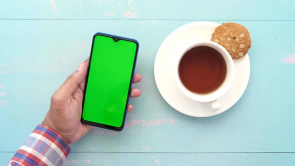 Young Man Hand Using Smart Phone with Tea and Cookies on Table