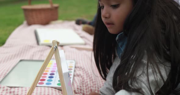 Little indian girl painting on small canvas at city park