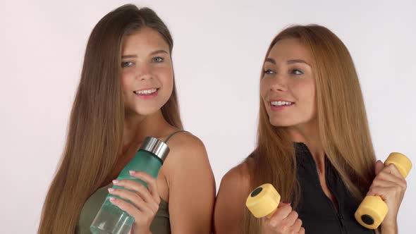 Two Fitness Women Smiling at Each Other, Posing with Water Bottle and Dumbbells