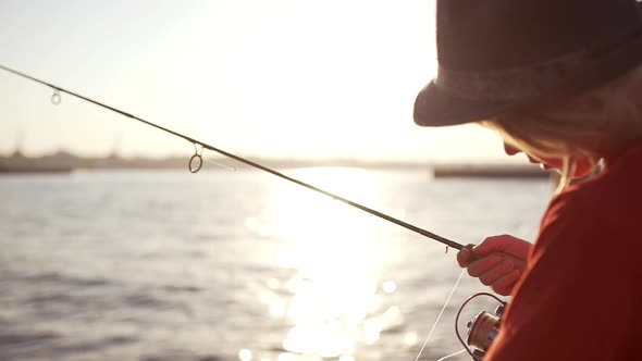 Young Caucasian Kid in Hat and Red Tshirt Checking His Fishing Rod Near Sea While Sun Shining in