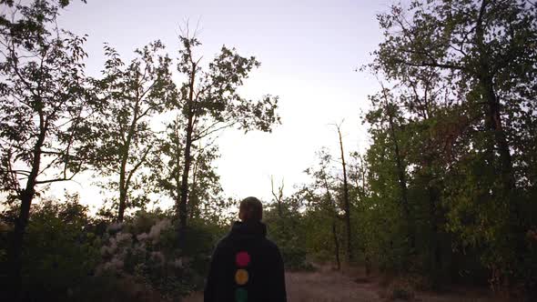 Young Man in Nice Hoodie with Tied Hair Strolling Through Forest During Sunset Looking Around View