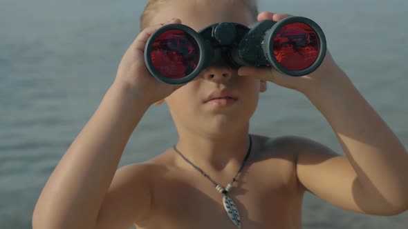 Slow motion view of small boy watching with binoculars against blurred sea