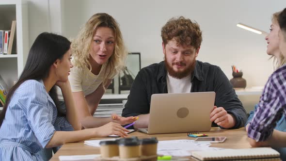 Group of Young Men and Women Sitting at Table in Modern Office and Discussing Business Issues in