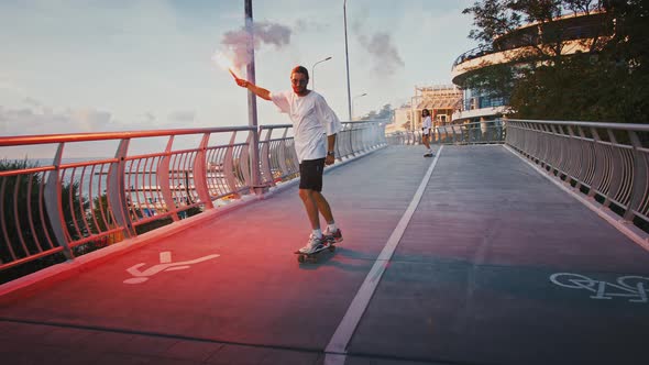 Young Man Riding Skateboard with Red Signal Fire Girlfriend Following Him Behind