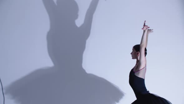 Young Woman Ballerina in Black Dress Dancing  a Big Shadow on the Wall