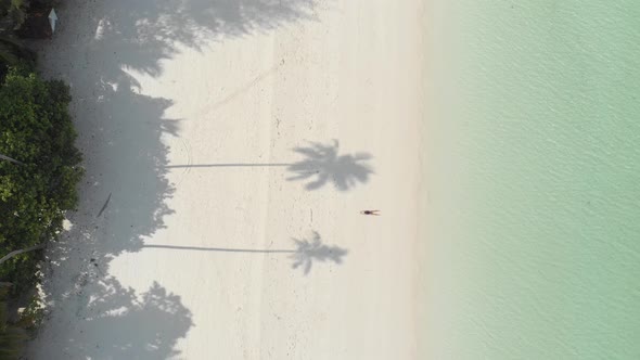 Aerial: Woman relaxing on white sand beach turquoise water tropical coastline