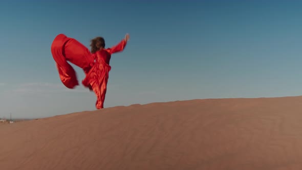 An Asian Woman in a Red Dress Dancing on Sand Dunes