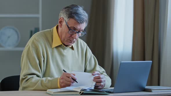 Multitasking Retired Caucasian Teacher Professor Senior Mature Man in Eyeglasses Looking at Laptop