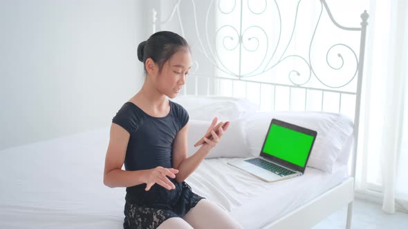 Asian ballet girl sit on bed with green screen laptop and enjoy to see example of ballet course