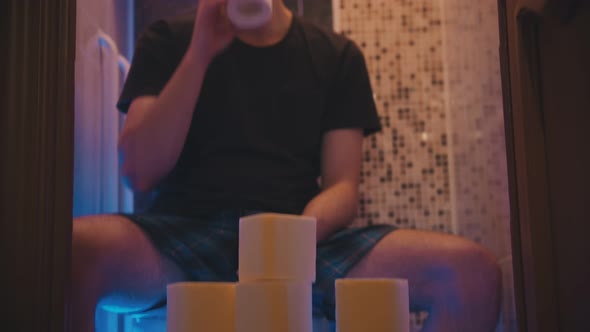 A Young Man Sitting on a Toilet with a Bunch of Toilet Paper