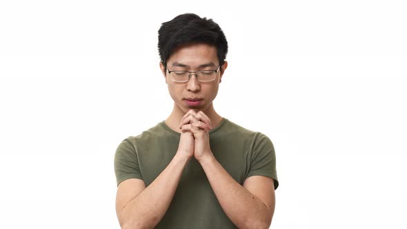 Portrait of Young Asian Man Wearing Glasses and Basic Tshirt Putting Hands Together and Praying with