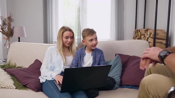 Wife and Her Cheery Son Sitting Together and Using Laptop and Greeting with High Five