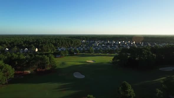 Drone flying over golf course towards houses during early morning