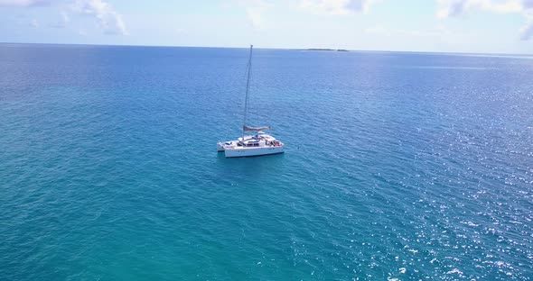 White catamaran anchoring on blue azure calm waters next to tropical island with resorts and villas