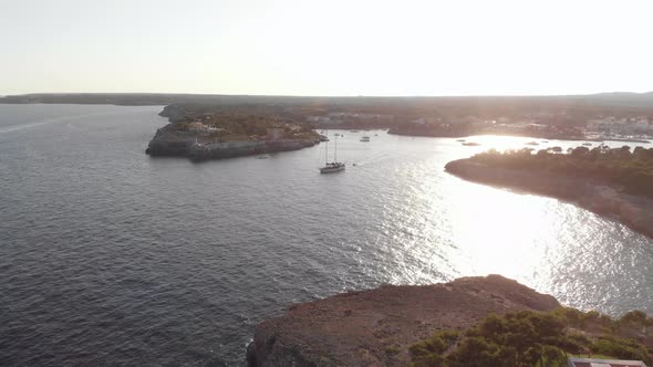 AERIAL: Mallorca coast at sunset and Sail Yacht float out of harbor bay