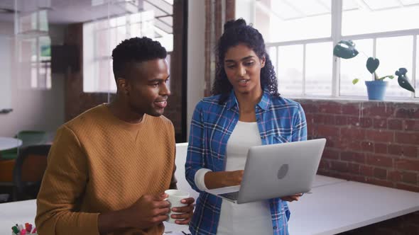 Diverse female and male business colleagues in discussion at work looking at laptop