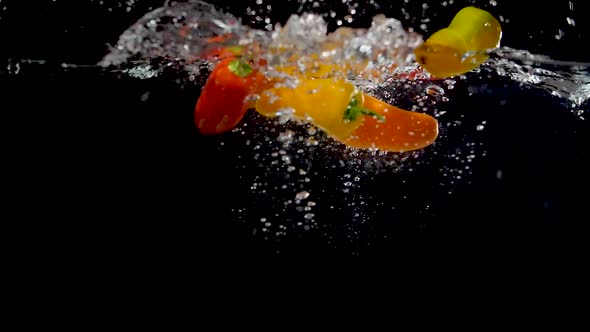 Colorful sweet peppers being dropped into water in slow motion.