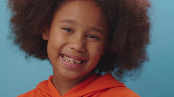 Portrait of African American girl in orange clothes smiling at camera on blue background