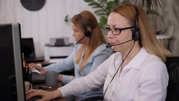 Two Women Talking to Clients on Headphones in a Call Center Office