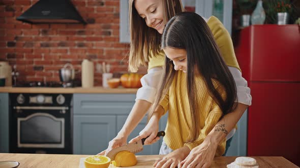 Smiling Little Girl Cutting Orange Standing By Table in Modern Kitchen at Home