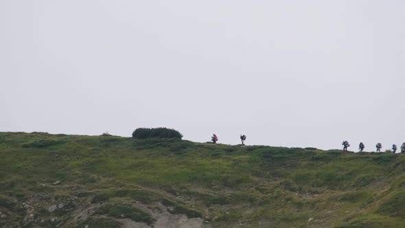 Group of Tourists with Hiking Backpacks Climbs the Mountain Range. Afar View