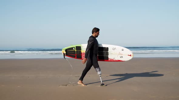 Side View of Happy Surfer with Disability Going Along Coastline