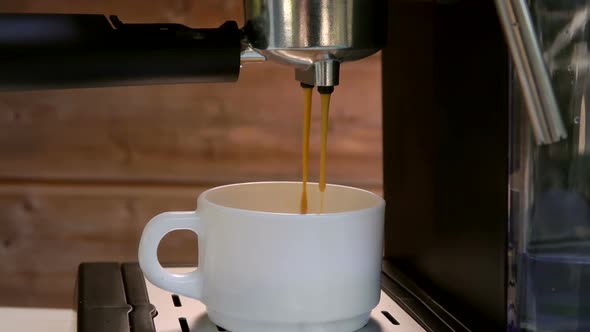 Stream of Fresh Coffee are Falling Into a White Cup From a Black Coffee Machine
