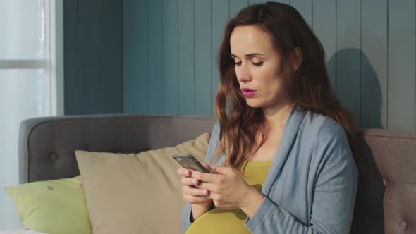 Portrait of Focused Pregnant Woman Chatting on Smartphone at Home