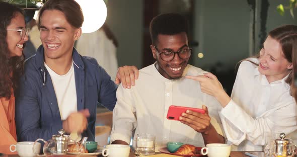 Afro American Young Man Holding Phone in Horizontal Landscape Mode While Showing Friends Funny Video