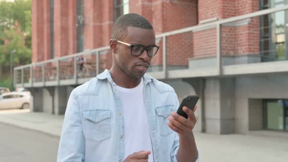 African Man Reacting to Loss on Smartphone While Walking in Street