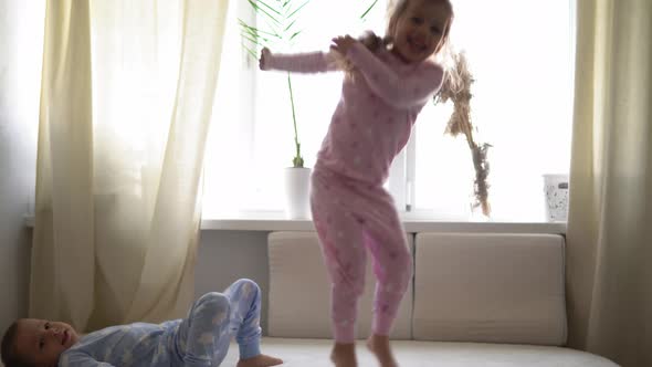 Two Smiling Preshool Toddler Children Boy and Girl Lieing on Back in Pajamas on White Bed