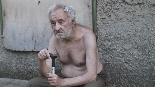 Sad Old Beggar Man with a Cane Sitting on the Street