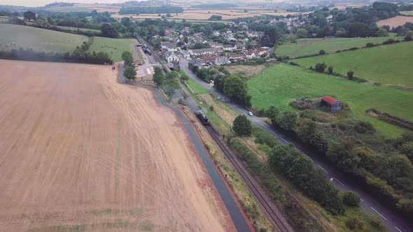 Aerial wide tracking forward over a Steam engine stationary that has pulled into a small station in