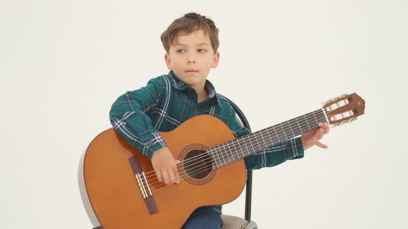 Little Boy is Playing Big Classical Guitar Sitting on the Stool